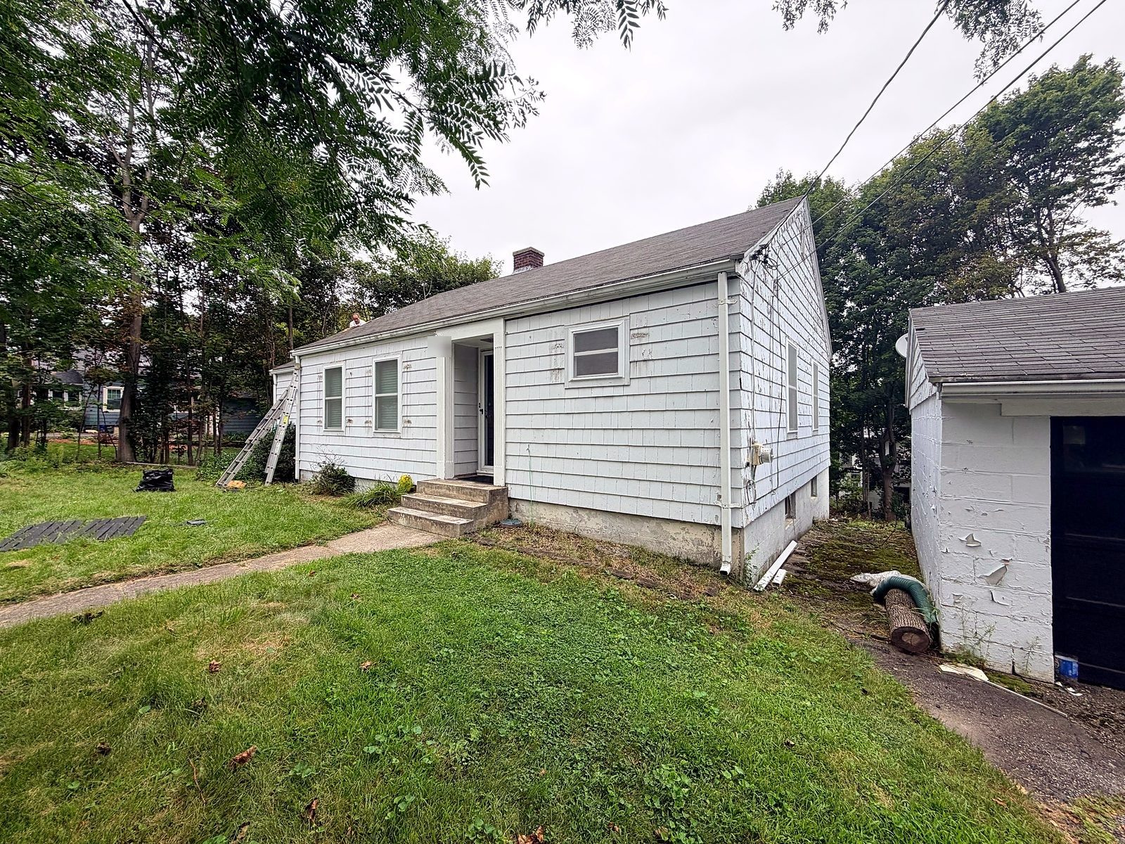 Small cape in Worcester, MA before rot repair — stained paint and failing shingles along the eave, ladders set for inspection